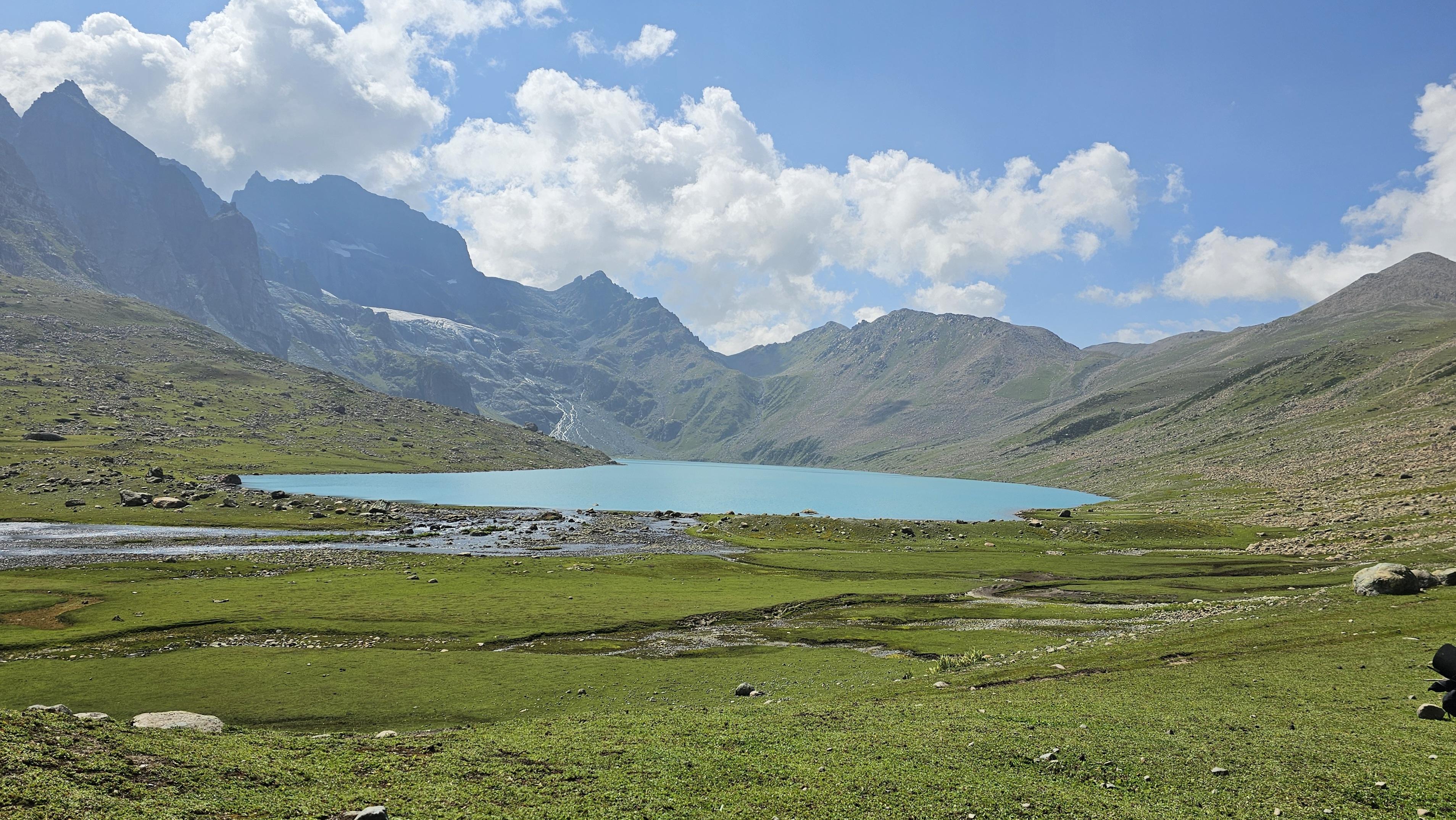 Meadows roll down toward the water below a pass.
